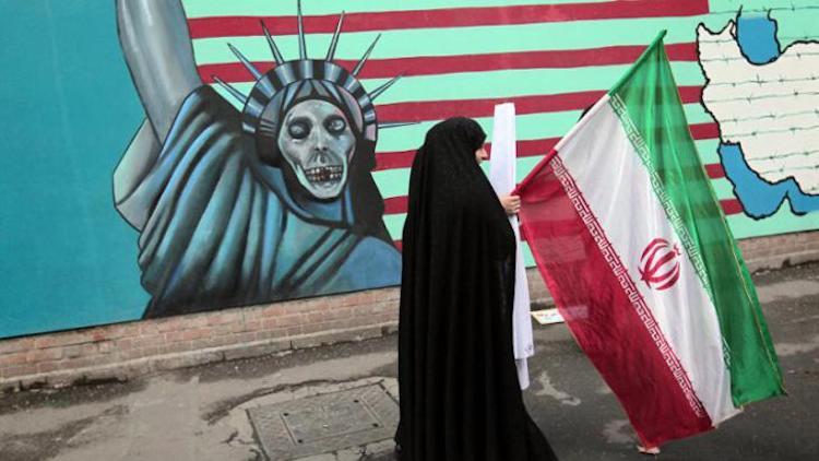 Photo: A woman passing by a painting on a wall of the former US embassy in Tehran in 2004 showing the US as a Satan. Credit: Behrouz Mehri